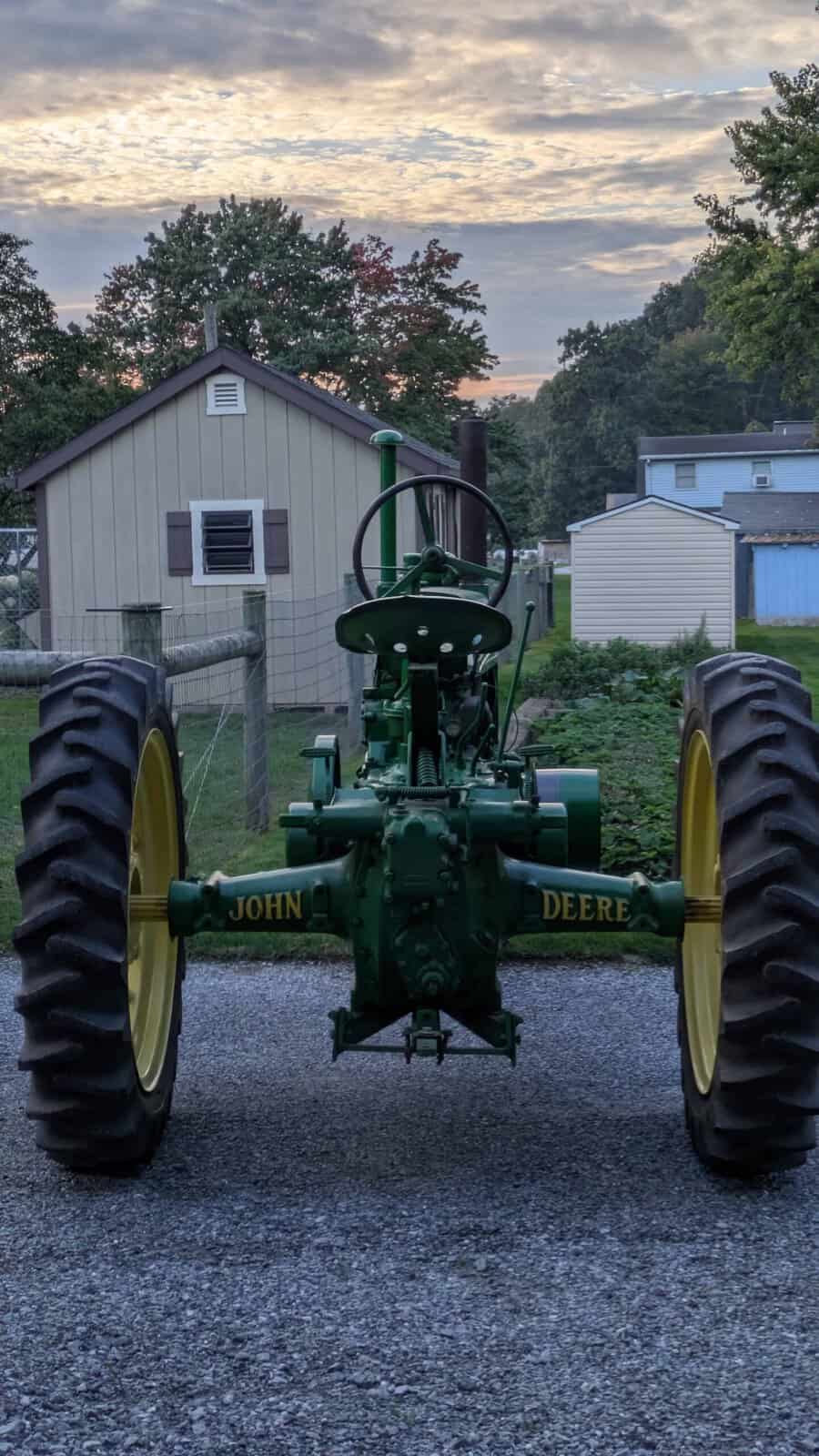 4456 (1) 1938 John Deere A tractor with large rear tires and green body, parked outdoors at sunset.
