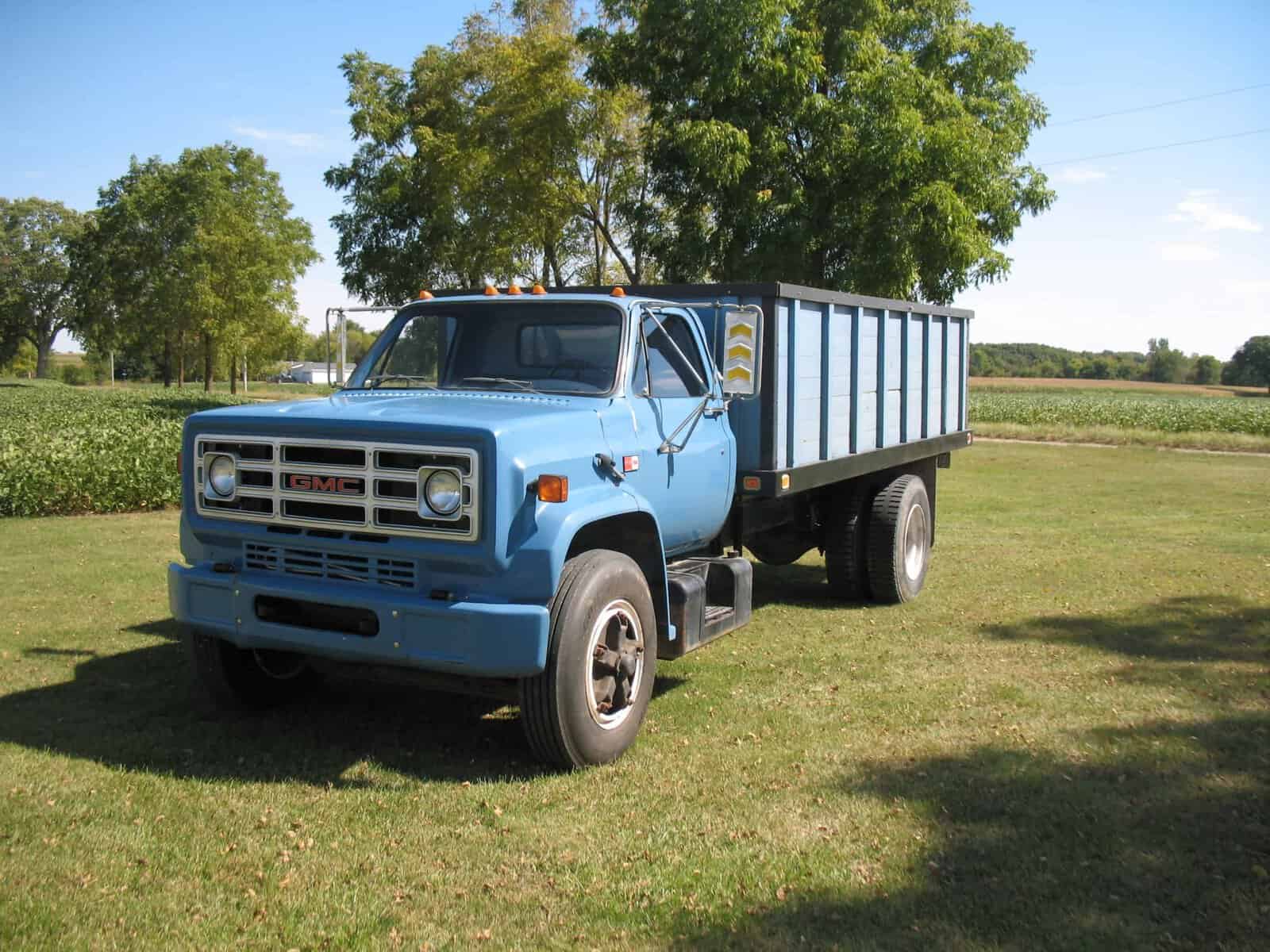 1985 GMC C7000 Dump Truck 1985 GMC C7000 dump truck blue with long bed and cab, front grille, dual rear wheels, on grassy field.