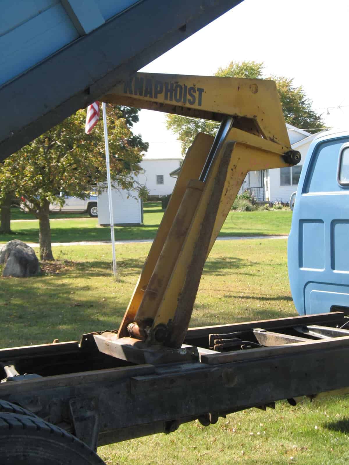 1985 GMC C7000 truck cab hoist arm Close-up of yellow hydraulic boom on a vintage GMC C7000 truck chassis.