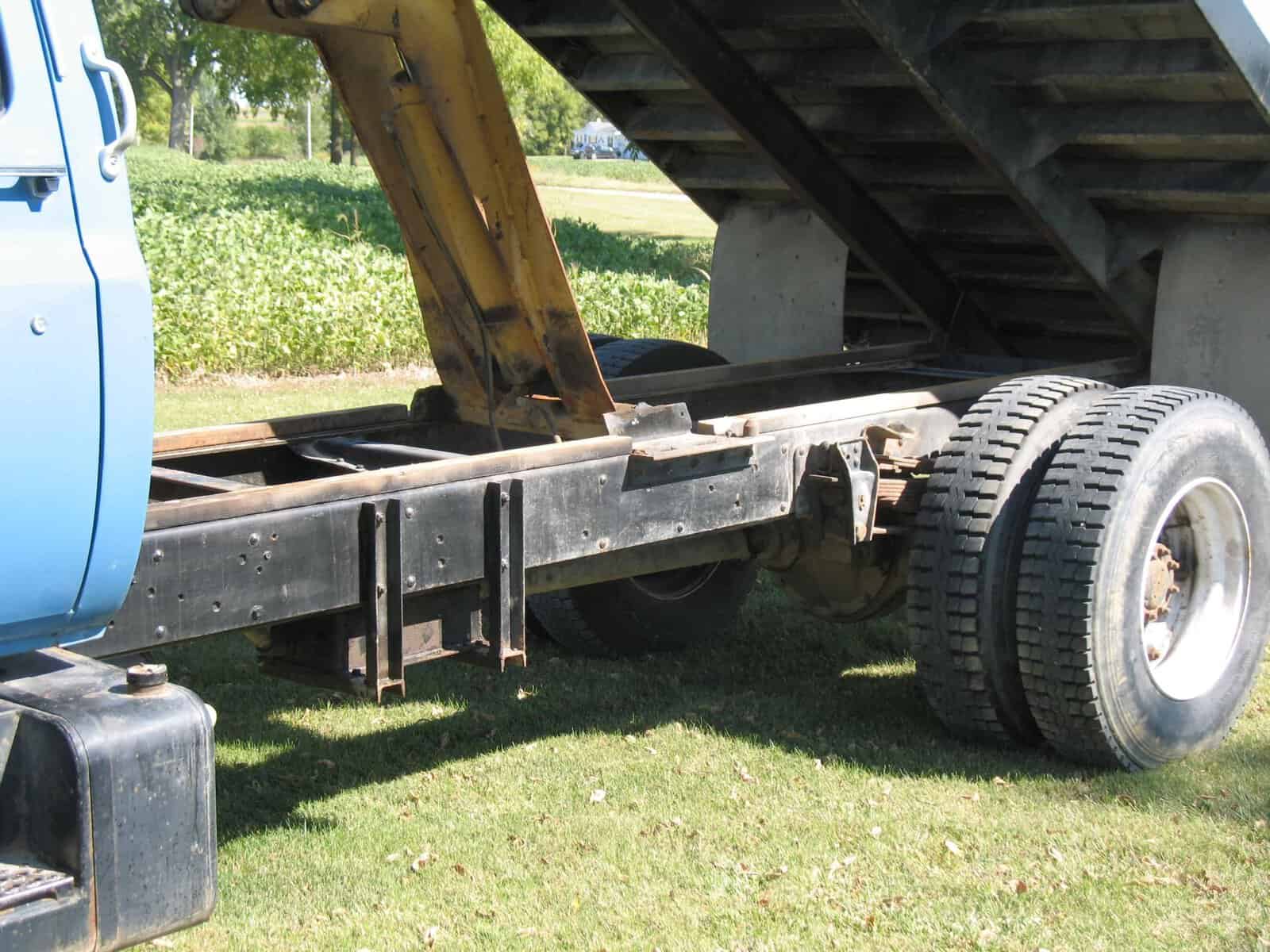 1985 GMC C7000 Grain Truck chassis 1985 GMC C7000 grain truck chassis with raised bed and dual rear tires on a grassy field.