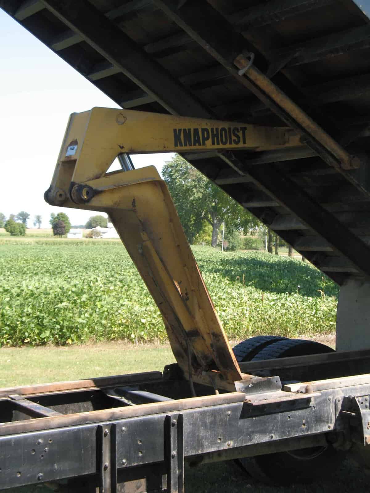 Knaphosit Excavator Arm Under Truck Bed Knaphosit excavator arm attached to a truck bed, yellow metal, undercarriage visible.