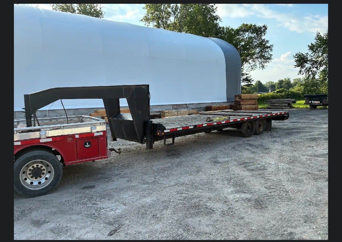 2018 BWise gooseneck tilt trailer with red cab and long flatbed, dual rear axles, in outdoor lot.