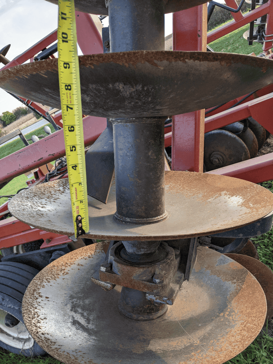 Versatile TD500 auger sizer disc depth Close-up of auger discs and spindle on agricultural equipment showing rust and measurement tape.