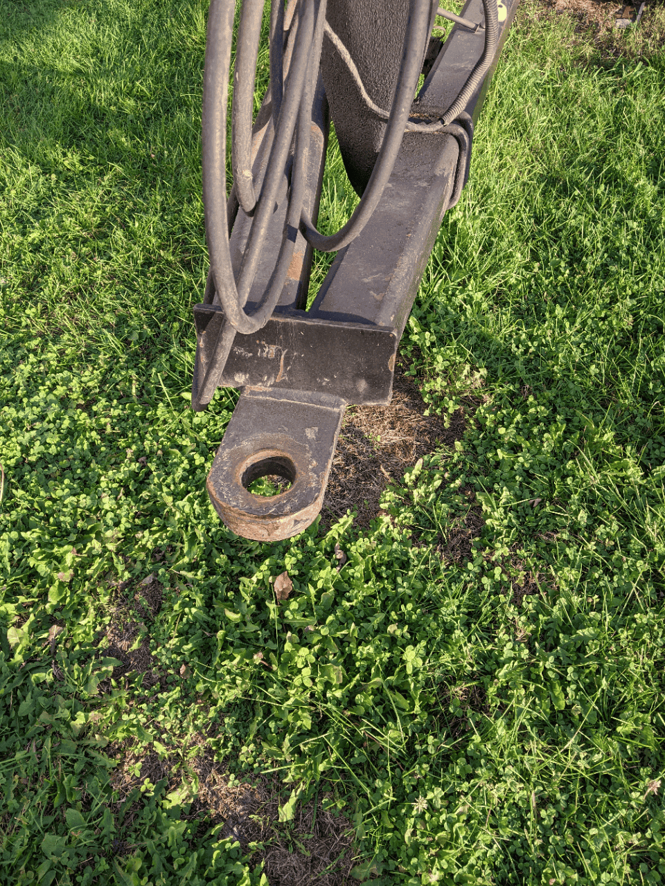 Tractor hitch with pin and hydraulic lines Front hitch and hydraulic connections on heavy equipment in grassy area.