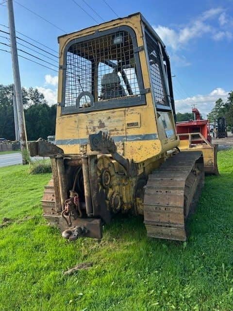 RAW_JD 650H 5 Yellow tracked skid steer loader with protective cage and visible wear, parked on grass.