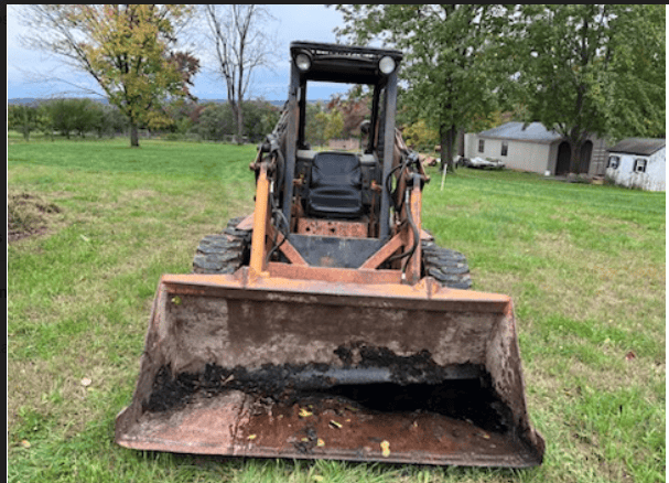 Case 1845 Skid Steer Loader with Bucket Front view of a used Case 1845 skid steer loader with bucket attachment on grassy field.