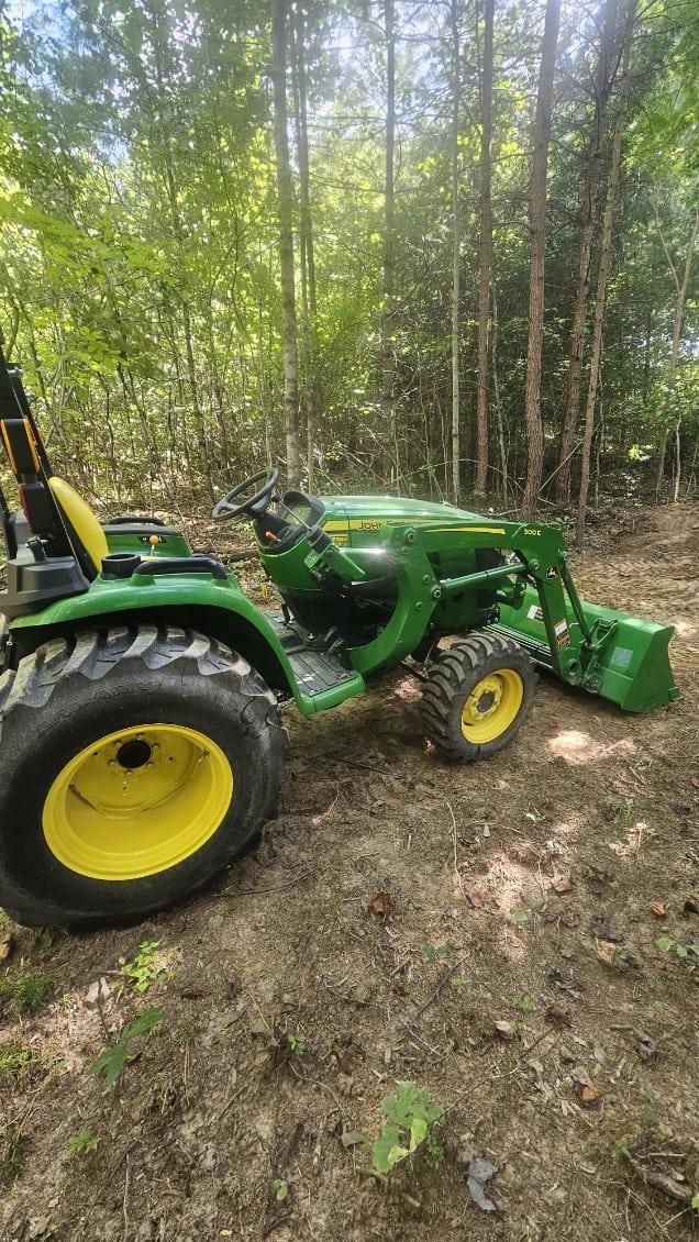 image000000 (9) Green John Deere 3025E compact tractor with front loader attachment in a wooded area.