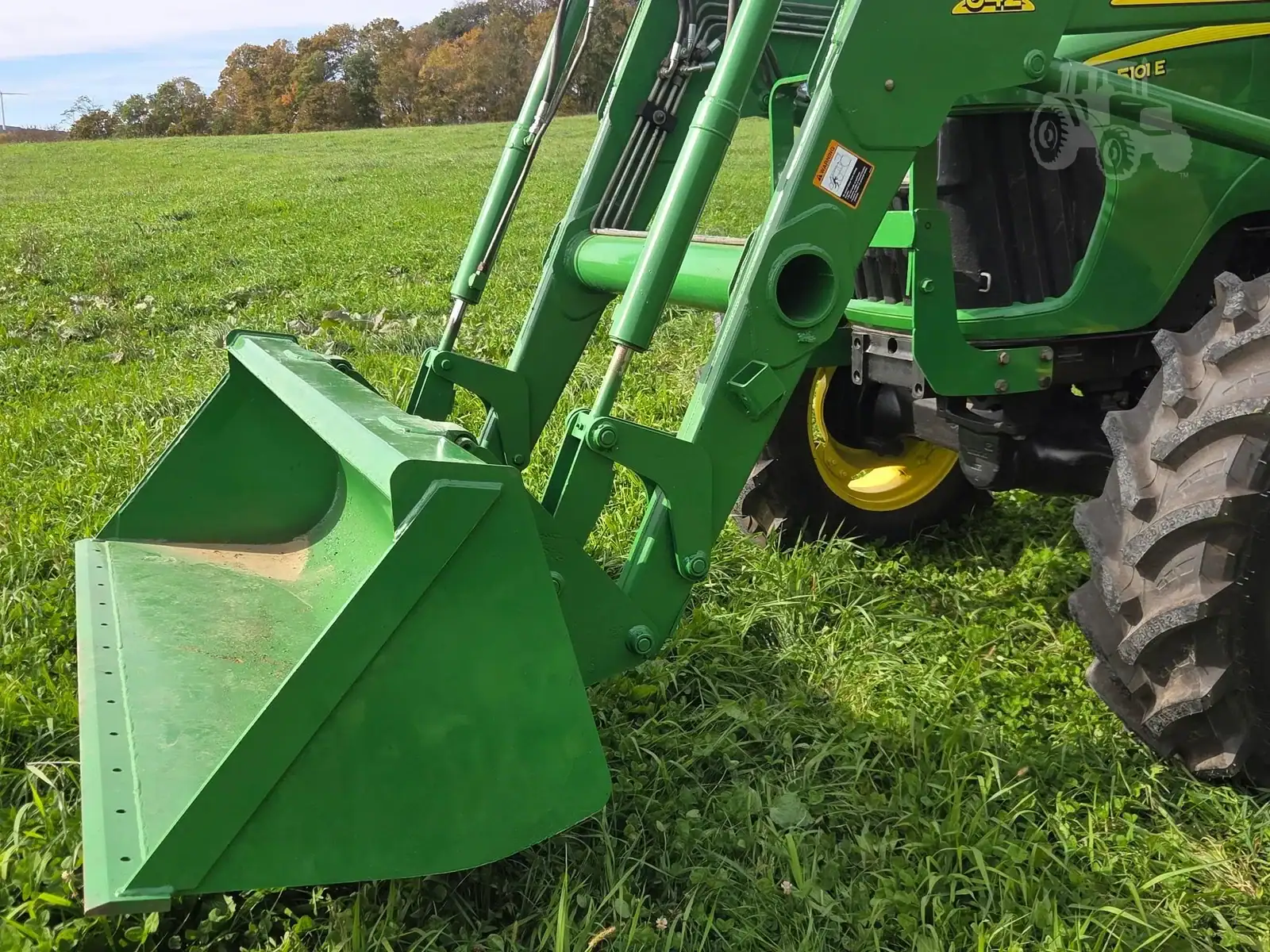 img (10) Green John Deere front loader attachment on a tractor in a grassy field.