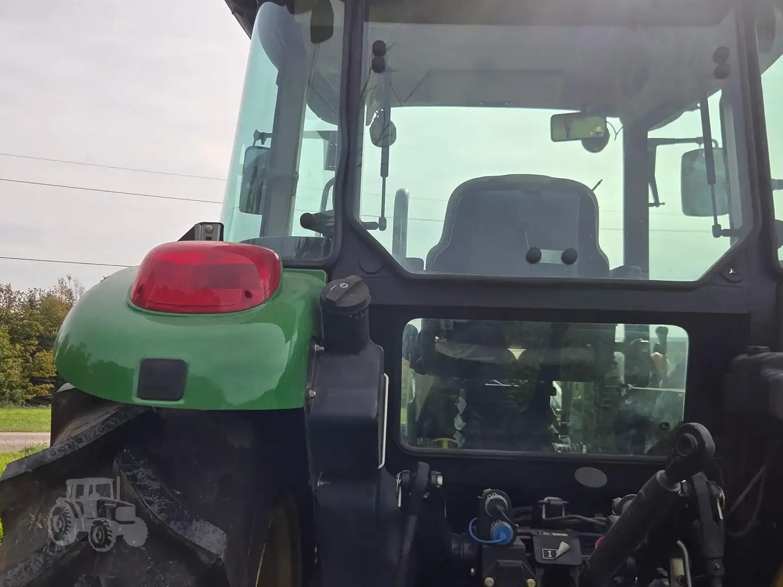 img (5) Green and black tractor with enclosed cab and red warning light on top, front view.