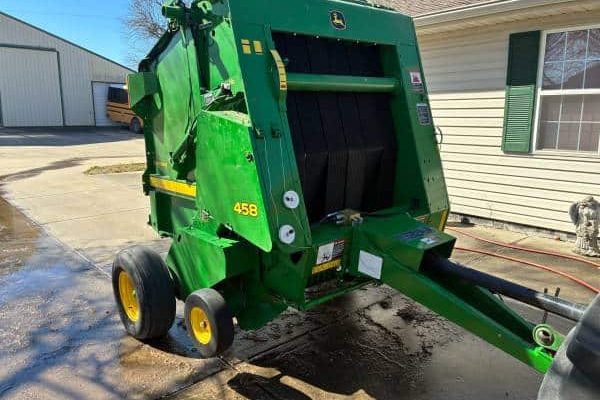 John Deere 458 bale wrapper with green body and black rollers, yellow wheels, and hitch for attachment.