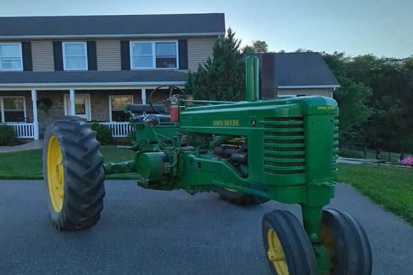Green vintage John Deere tractor with yellow wheels parked on driveway near house.
