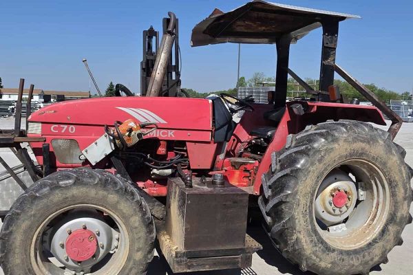 Red McCormick C70 tractor with canopy and large tires on a farm lot.