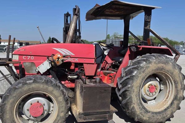 Red McCormick C70 tractor with canopy and large tires on a farm lot.