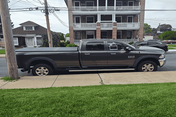 Black 2014 RAM 2500 Big Horn pickup truck parked on street in front of a multi-story building.