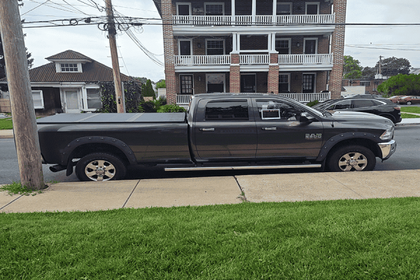 Black 2014 RAM 2500 Big Horn pickup truck parked on street in front of a multi-story building.
