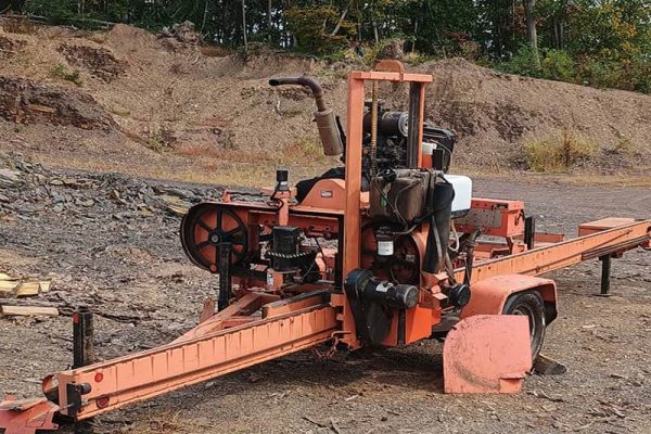 Wood-Mizer LT40 hydraulic sawmill with orange frame and cutting bed on uneven ground.