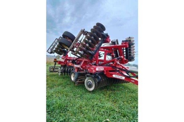 Red 2022 Case IH farm disc harrow with multiple disc blades and large tires on green field under cloudy sky.