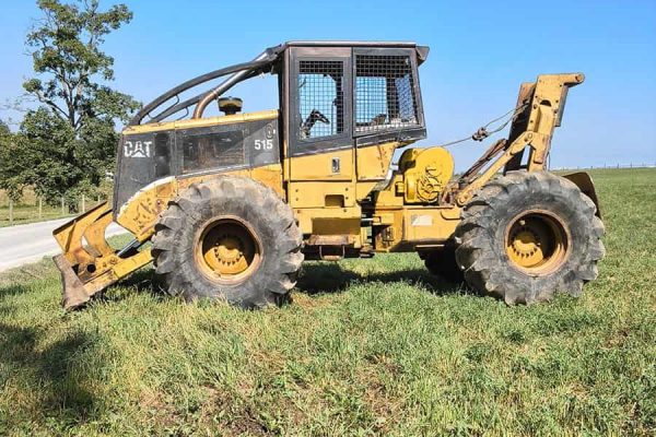 Caterpillar 515 skid steer loader with yellow body and black cab on grassy field under blue sky.