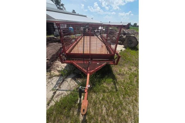 Red utility trailer with mesh sides and wooden floor, parked outdoors on grass.