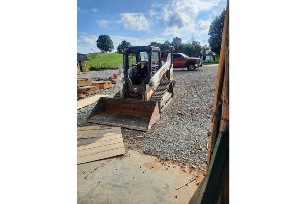 Excavator with a front bucket attachment parked outdoors on a gravel surface in a rural setting.