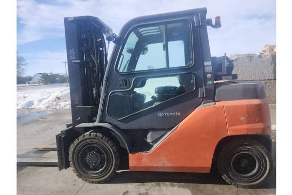 Toyota forklift, orange and black, side view, outdoor setting with snow and clear sky.