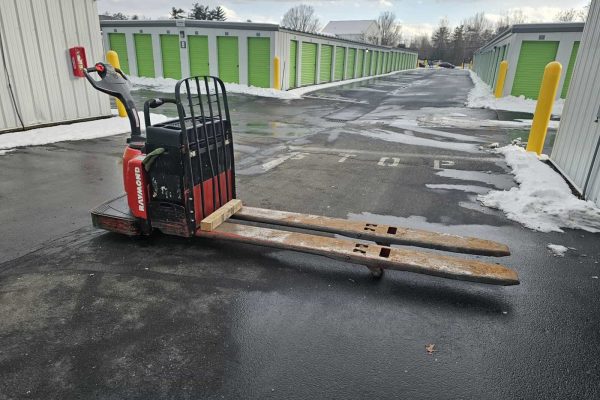 2006 Raymond 8400 electric pallet jack with black handle and red body on wet asphalt in storage facility.