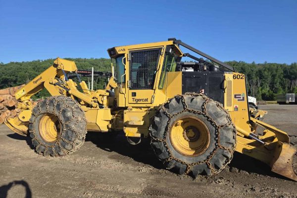John Deere 602 Tigercat forestry skidder with large tires and cab, yellow and black color, on a dirt lot.