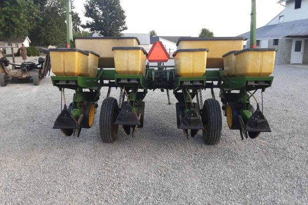 John Deere 7000 planter with yellow seed hoppers and black row units on gravel surface.