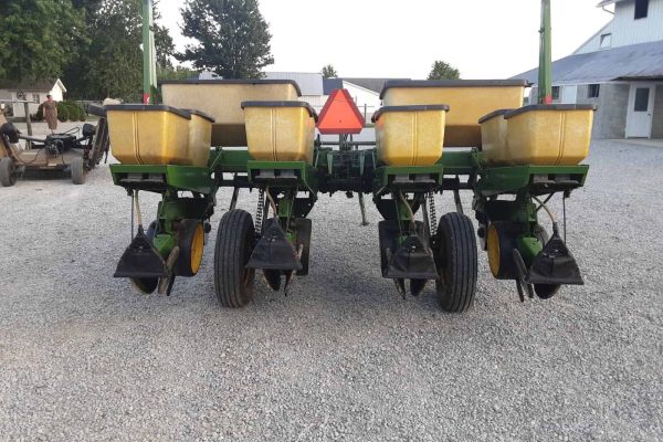 John Deere 7000 planter with yellow seed hoppers and black row units on gravel surface.