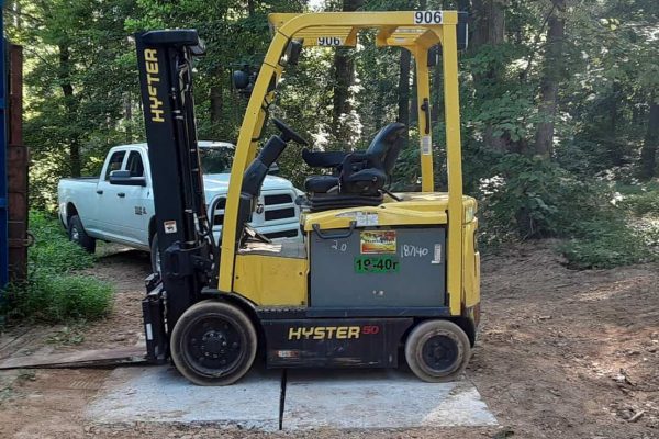 Yellow Hyster E50XM forklift with black mast and tires, parked on dirt near trees and a blue shipping container.