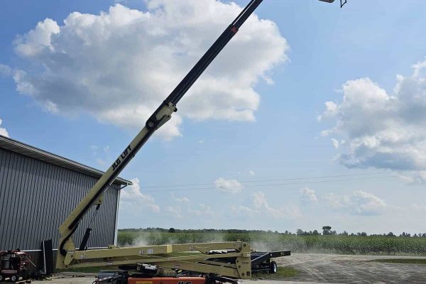 2015 JLG X700AJ boom lift with extended arm and basket, outdoor setting under blue sky with clouds.