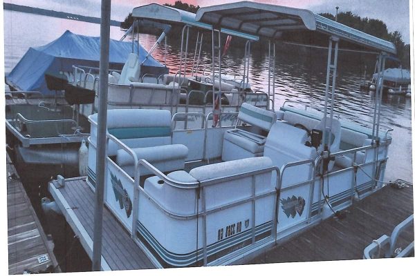 Suncruiser pontoon boat with canopy, seating, and safety rails on dock at sunset.