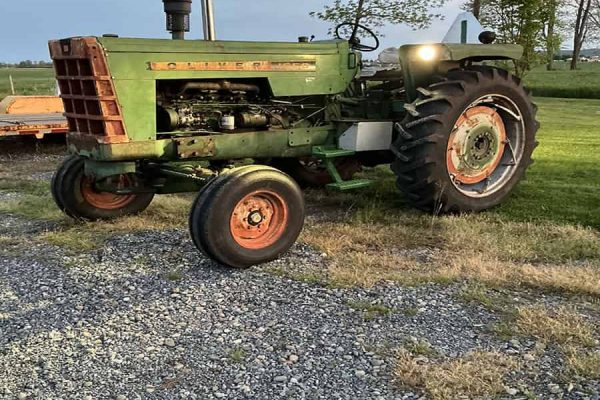 Green Oliver 1550 tractor with front loader and large rear tires on grassy field.