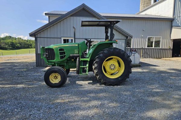 Green John Deere 6100D tractor with cab and large rear tires on gravel surface.
