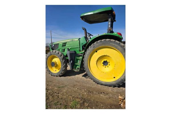 Green John Deere tractor with yellow wheels, no visible model year, on a farm field under a clear blue sky.