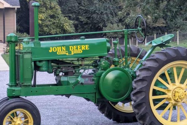 1938 John Deere A tractor with green body and yellow wheels on a gravel driveway.
