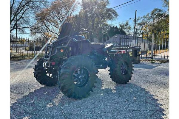 All-Terrain Utility Vehicle (UTV) with black body and large tires, parked outdoors on gravel surface.
