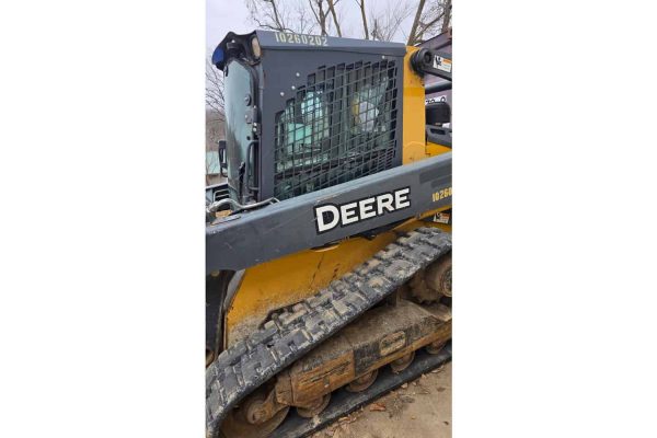 DEERE 1025R compact tractor with enclosed cab and rubber tracks, ideal for landscaping and small farm tasks.