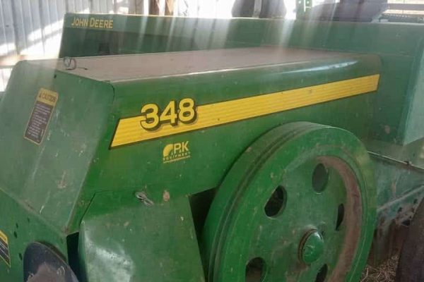 John Deere 348 square baler, green and yellow, stored indoors.