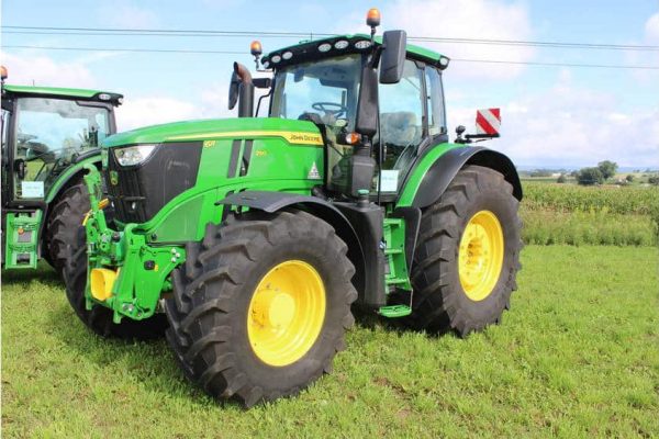 Green John Deere 8R Series tractor with large tires, parked on grassy field under blue sky.