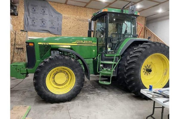John Deere 6110 tractor, green and yellow, inside a workshop with tools and equipment.