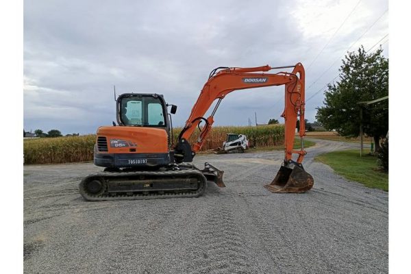 Ducati mini excavator, orange, on gravel surface with cloudy sky background.