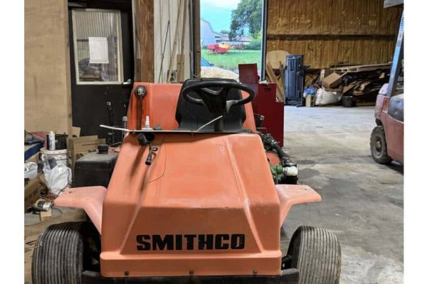Compact orange Smithco ride-on lawn mower in a workshop setting.