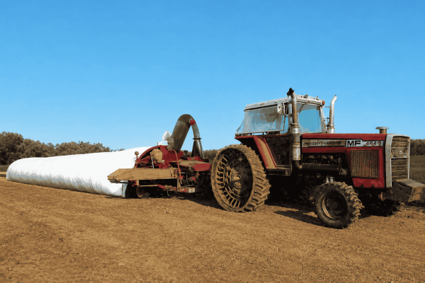 Massey Ferguson 2745 tractor with hay baler attachment on a farm field under clear blue sky.