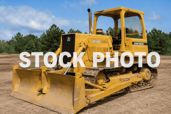 John Deere 450D crawler dozer with blade and tracks on dirt under blue sky.