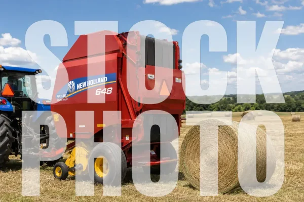 New Holland 648 round baler in a field with blue sky and clouds.