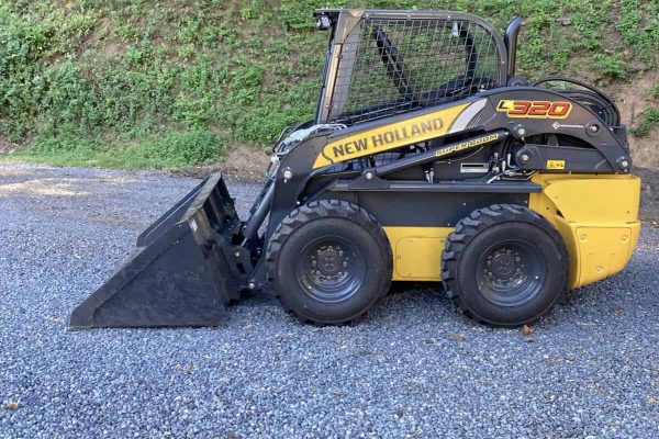 New Holland L320 skid steer loader with black and yellow body and bucket attachment on gravel surface.