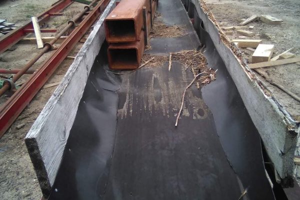 Heavy-duty metal channel with orange pipes on a construction site, surrounded by wood and metal materials.