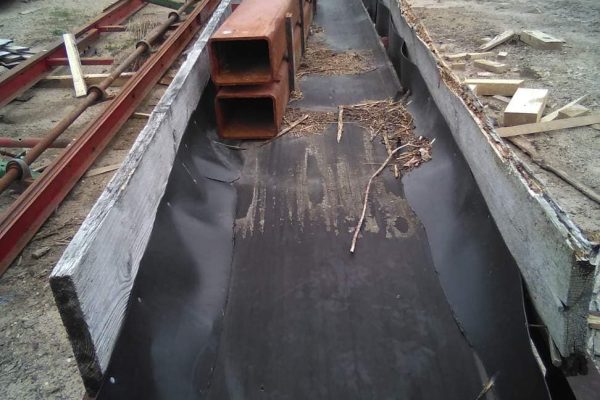 Heavy-duty metal channel with orange pipes on a construction site, surrounded by wood and metal materials.