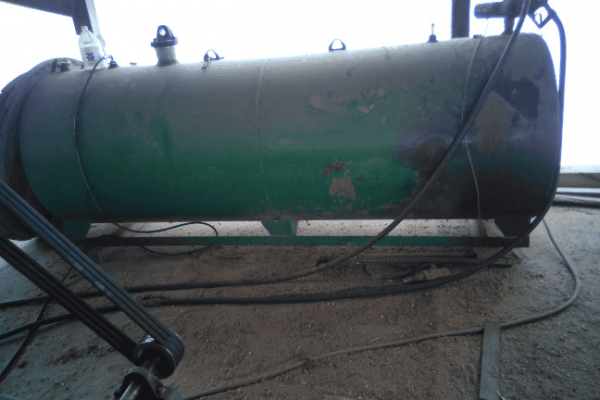 Green horizontal storage tank with valves and hoses, industrial setting, no identifiable year or model.
